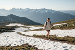 woman hiking wearing short and sweater, in a mountain with a bit of snow on the grond